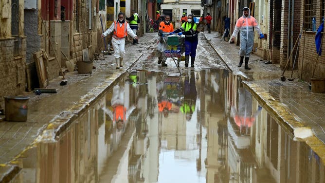 Agents wearing protective jumpsuits take part in cleaning works in a street covered in mud in Paiporta, south of Valencia, eastern Spain, on November 13, 2024 in the aftermath of deadly flooding. Spain closed schools and evacuated residents as heavy rains lashed the country on November 13, two weeks after its worst floods in a generation killed more than 200 people.